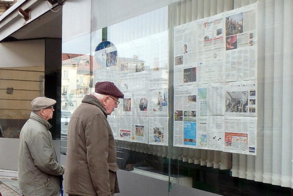 Guys reading some newspapers pasted in a window in Ljubljana.