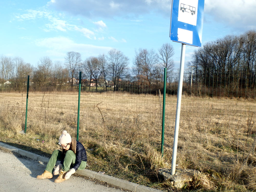 Masayo tying her shoe at a bus stop