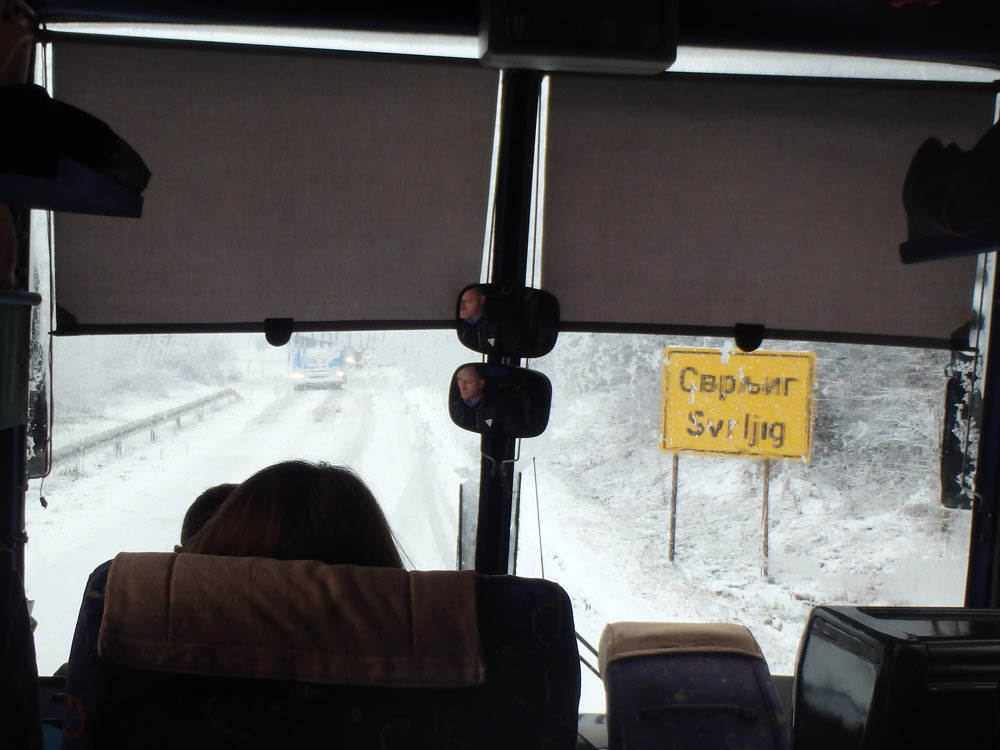 Snowy road out the bus window in Serbia. The truck and bus in the distance had both stopped and were reversing back into town. I think they had decided not to take the road — the one we had just come through. *Gulp*